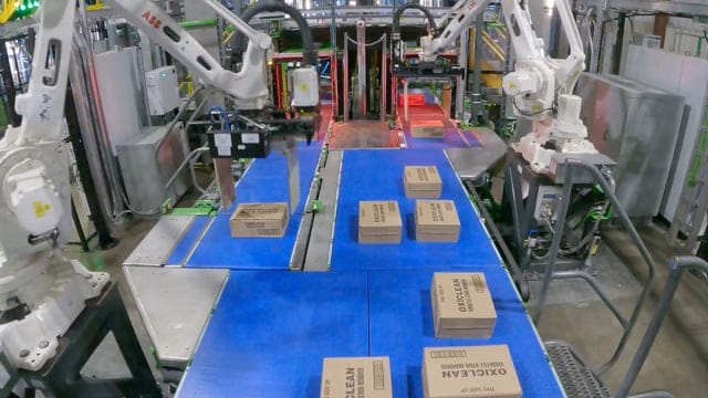 Robotic arms sorting packages on a conveyor belt in a warehouse setting, showcasing advanced automation technology.