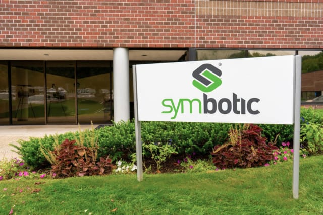 Symbotic company sign outside modern office building with landscaping and glass entrance.